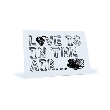 weiße Postkarte mit dem Spruch "Love is in the air"