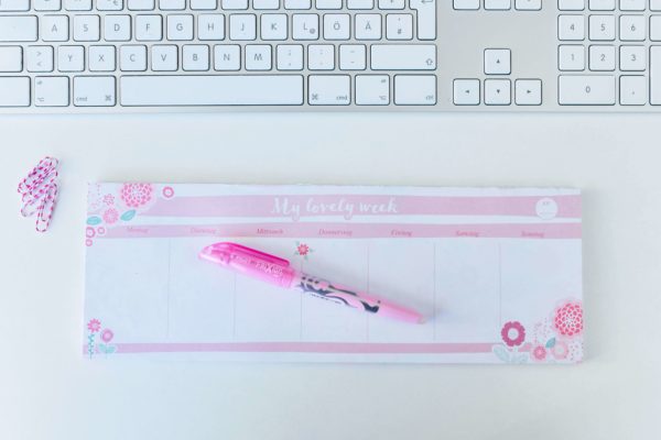 rosa Tischkalender mit Blumenmotiv, Tastatur, rosa Büroklammern und rosa Stift